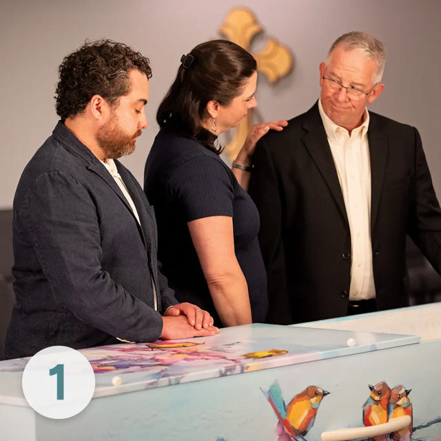 Three people in share a solemn moment around a LifeArt cremation container