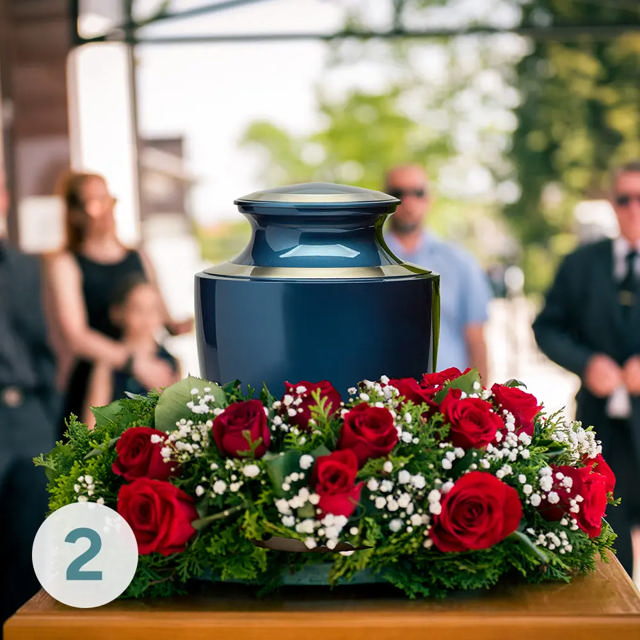 A blue urn surrounded by red flowers is displayed at a funeral