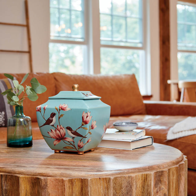 A pale blue urn with a birds and flowers sitting on a coffee table